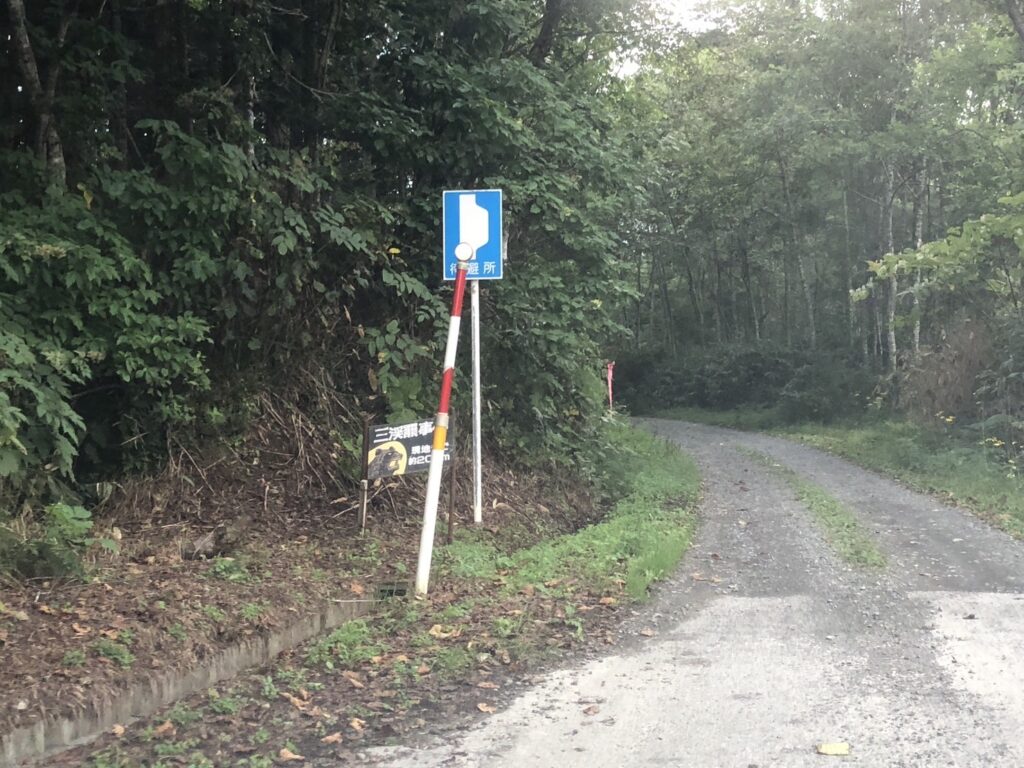 Gravel road and directional sign near the Sankebetsu Bear Attack Site, surrounded by quiet nature