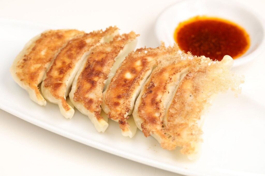 gyoza dumplings served with spicy red dipping sauce on white ceramic plate traditional cuisine