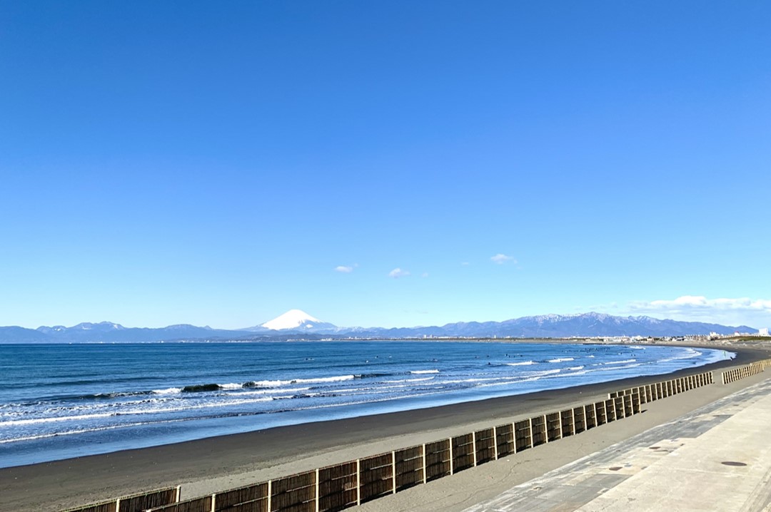 View of snow-capped Mount Fuji from a beach with waves and breakwater in the foreground