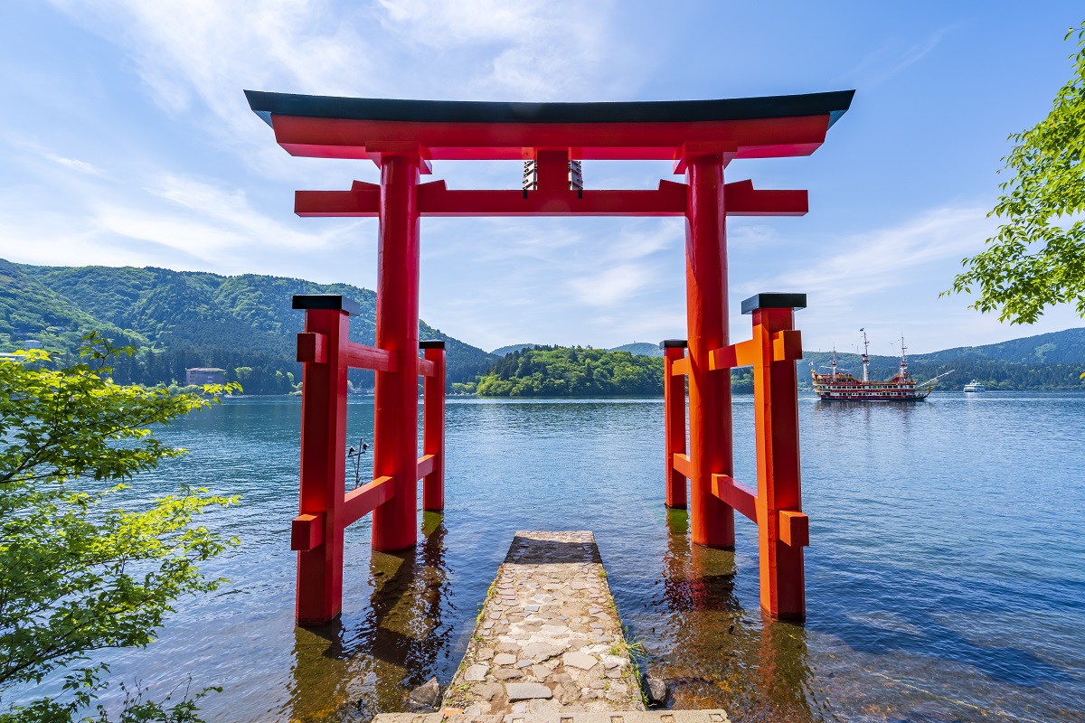 Red torii gate standing in Lake Ashi with a sightseeing pirate ship and mountains in the background