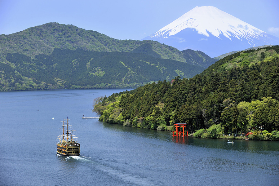 Scenic view of Lake Ashi with Mount Fuji, red torii gate, and sightseeing ship surrounded by forested mountains